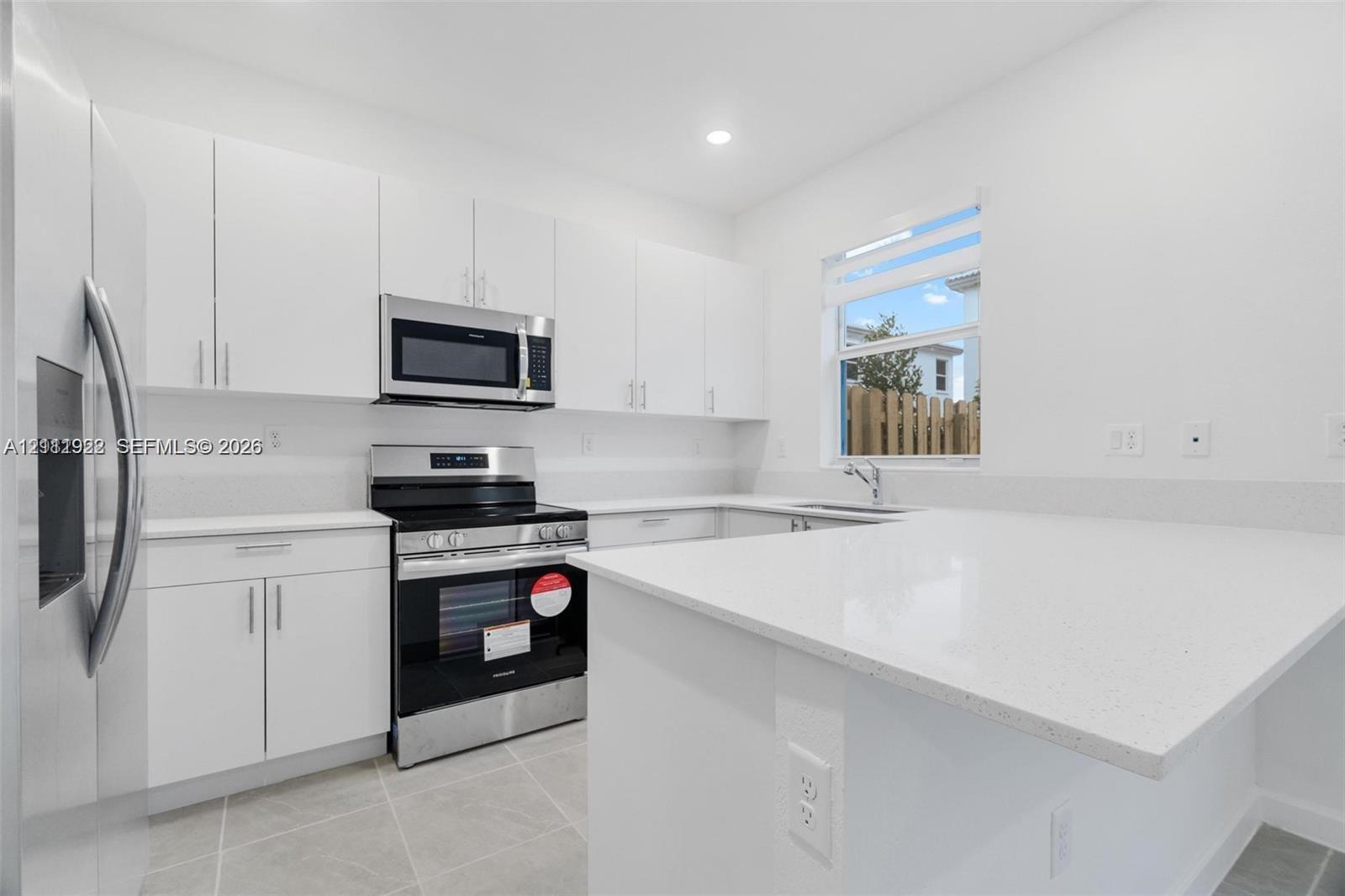 Kitchen featuring white flat-panel cabinetry, quartz countertops, a peninsula breakfast bar, stainless steel appliances, and large-format tile flooring Kitchen featuring white flat-panel cabinetry, quartz countertops, a peninsula breakfast bar, stainless steel appliances, and large-format tile flooring