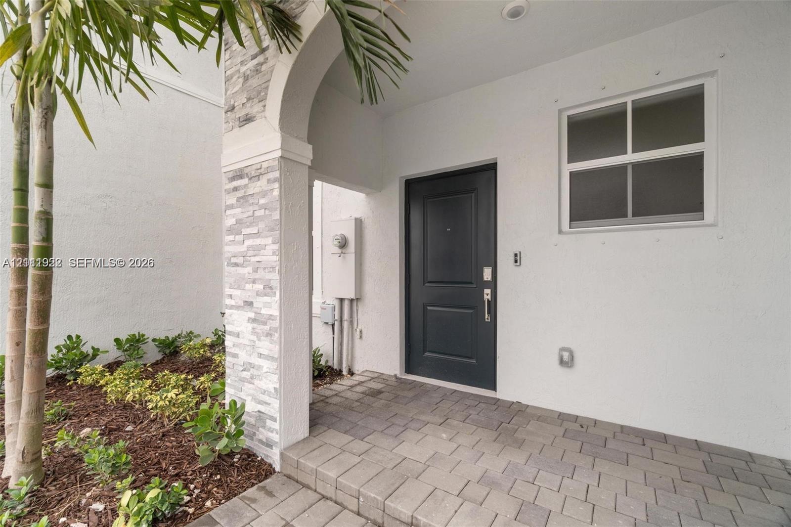 Covered entryway featuring a stone-clad arched pillar, paved flooring, and a solid-panel front door Covered entryway featuring a stone-clad arched pillar, paved flooring, and a solid-panel front door