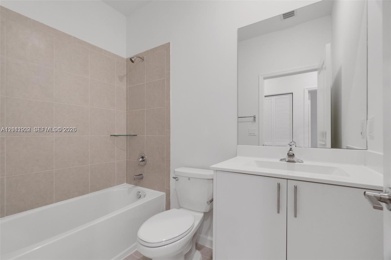 Bathroom featuring a white vanity cabinet with a stone countertop, an integrated sink with a chrome faucet, a frameless wall-mounted mirror, and a tub-shower combination with neutral tile surround