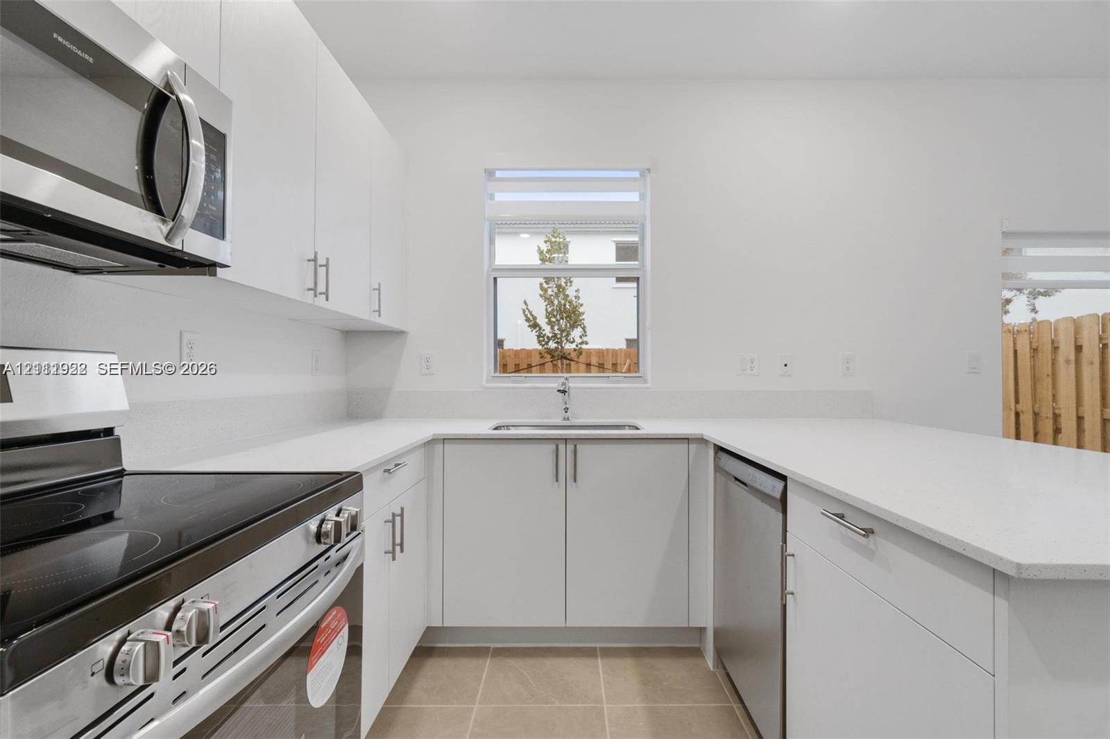 Kitchen featuring flat-panel white cabinetry, stone-surface countertops, stainless steel appliances, and tile flooring Kitchen featuring flat-panel white cabinetry, stone-surface countertops, stainless steel appliances, and tile flooring