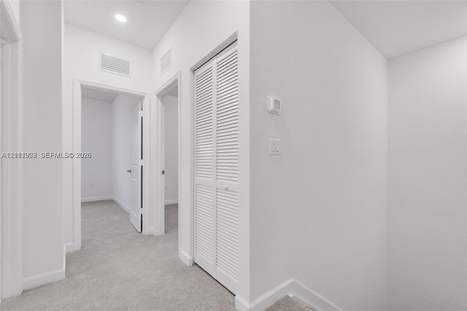 Interior hall featuring wall-to-wall carpeting, recessed ceiling lighting, and a closet with louvered double doors