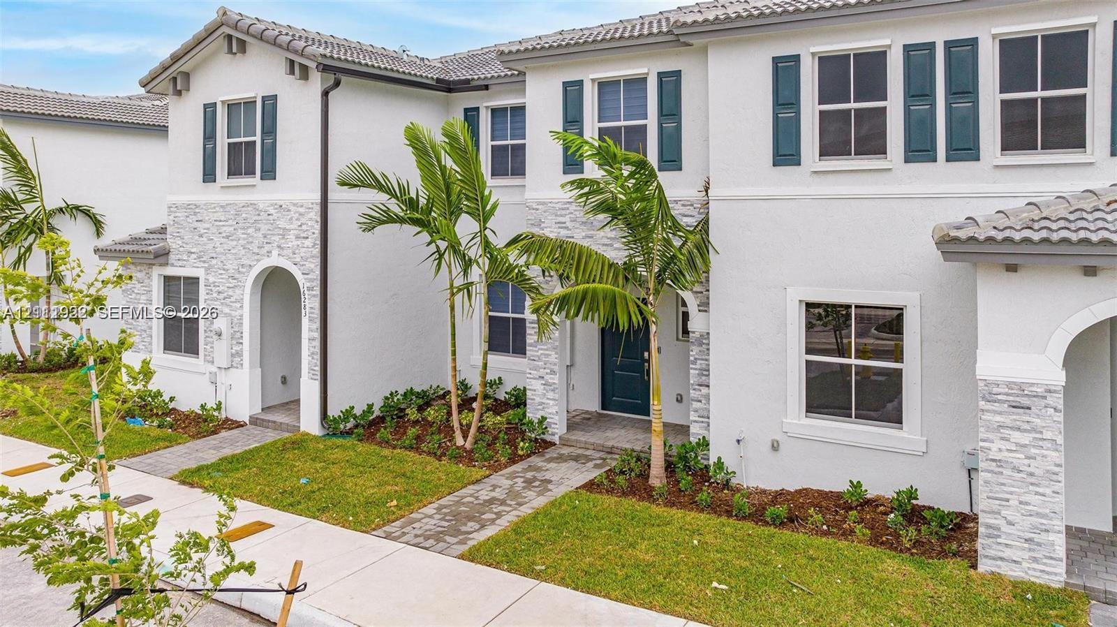 Stucco exterior with stacked stone veneer accents, multi-pane windows with decorative shutters, tiled roof, and paver walkways