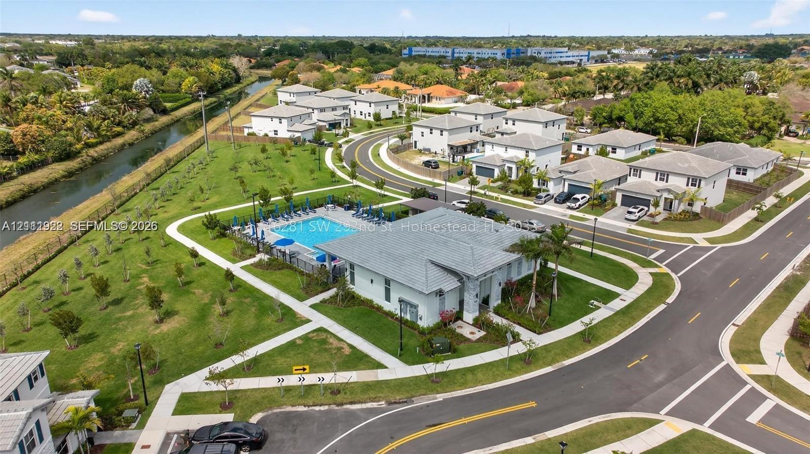 Aerial perspective of a community featuring a swimming pool, paved pedestrian walkways, expansive green space, and a water canal
