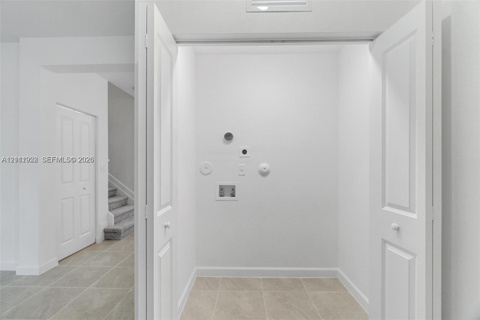 Dedicated utility area featuring bi-fold doors, tile flooring, and integrated plumbing hookups