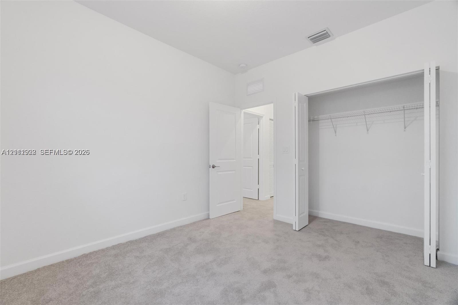 Neutral interior space featuring wall-to-wall carpeting, white walls, multi-panel interior doors, and a closet with integrated wire shelving