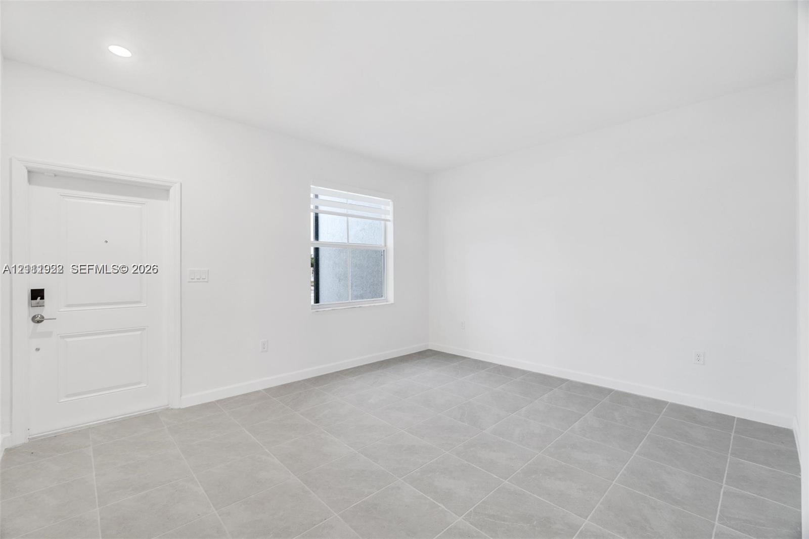 Neutral-toned interior space featuring tile flooring, smooth white walls, recessed ceiling lighting, and a single-panel entry door with integrated electronic lock Neutral-toned interior space featuring tile flooring, smooth white walls, recessed ceiling lighting, and a single-panel entry door with integrated electronic lock
