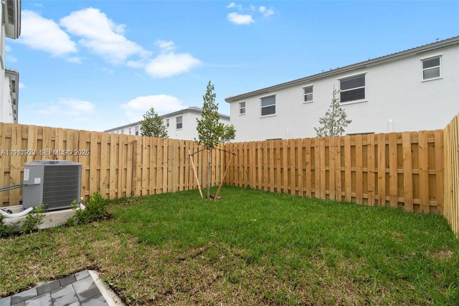 Enclosed backyard featuring a privacy wood fence, manicured lawn, young tree, and paver hardscaping