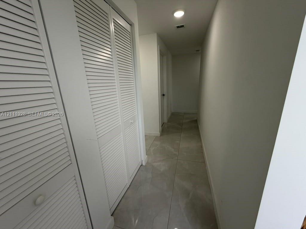 Hallway featuring large-format tile flooring and white louvered-door closet cabinetry