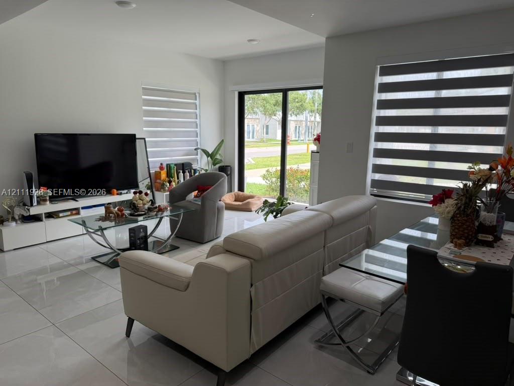 Open-concept interior featuring large-format tile flooring, sliding glass door, and zebra-style window treatments