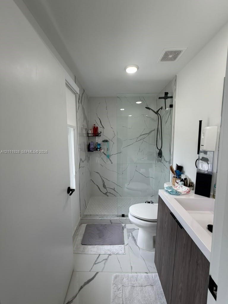 Bathroom featuring large-format tile flooring with marble-finish veining, a walk-in shower with a frameless glass enclosure, and a wood-finish vanity with a white countertop