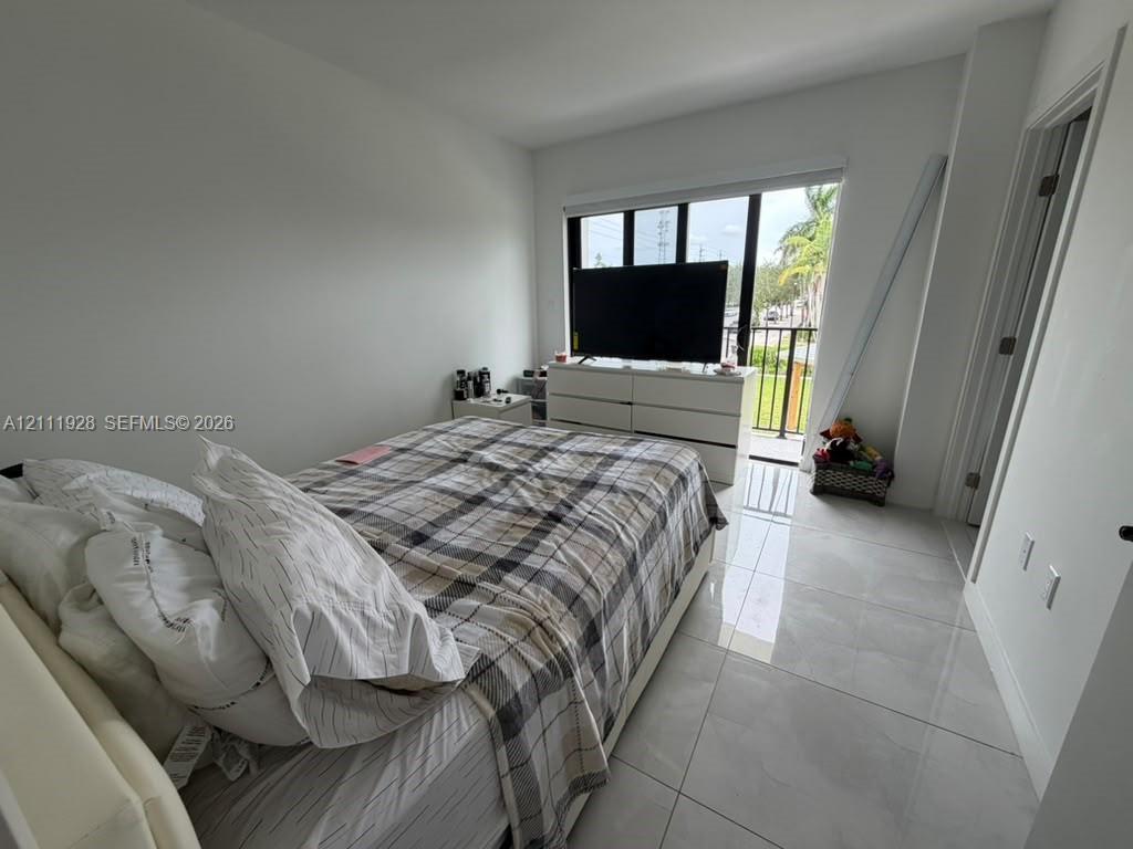 Room featuring large-format tile flooring, floor-to-ceiling windows, and a sliding glass door providing access to a private balcony