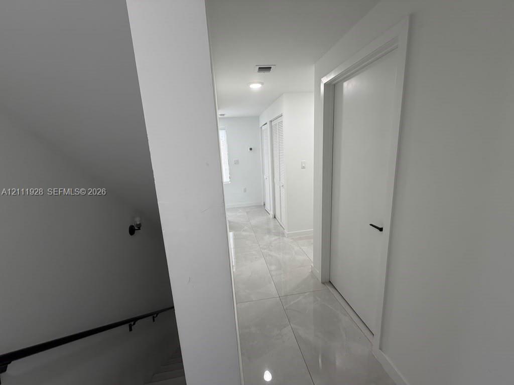 Large-format neutral stone-style tile flooring, solid-core doors with matte black hardware, and recessed lighting