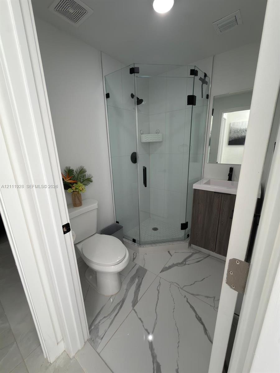Corner shower stall with glass enclosure and matte black hardware, vanity with stone-pattern countertop, and large-format porcelain tile flooring