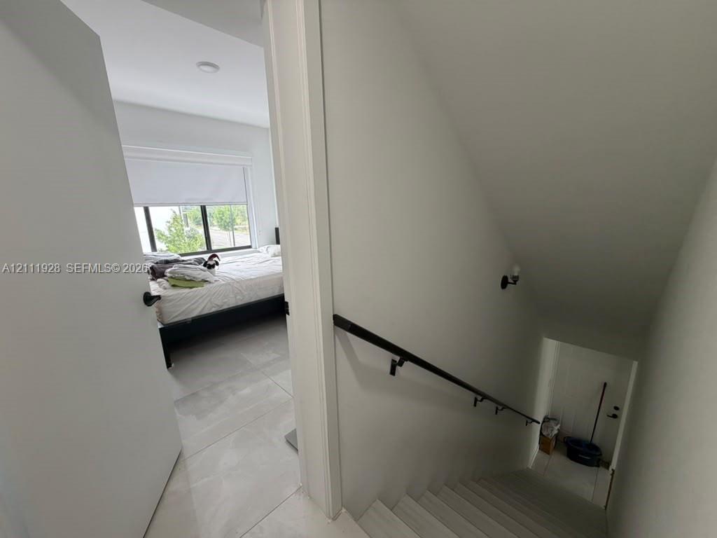 Neutral-toned interior featuring large-format tile flooring, a staircase with a matte black handrail, and recessed lighting