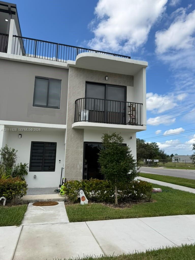Modern multi-story exterior featuring a rooftop deck, second-level balcony with metal railing, textured stone facade, and paved walkway