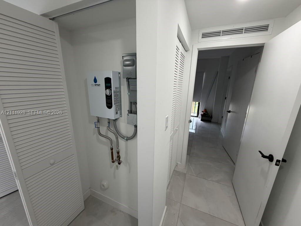 Utility alcove featuring a wall-mounted electric tankless water heater, white louvered closet doors, and large-format porcelain tile flooring