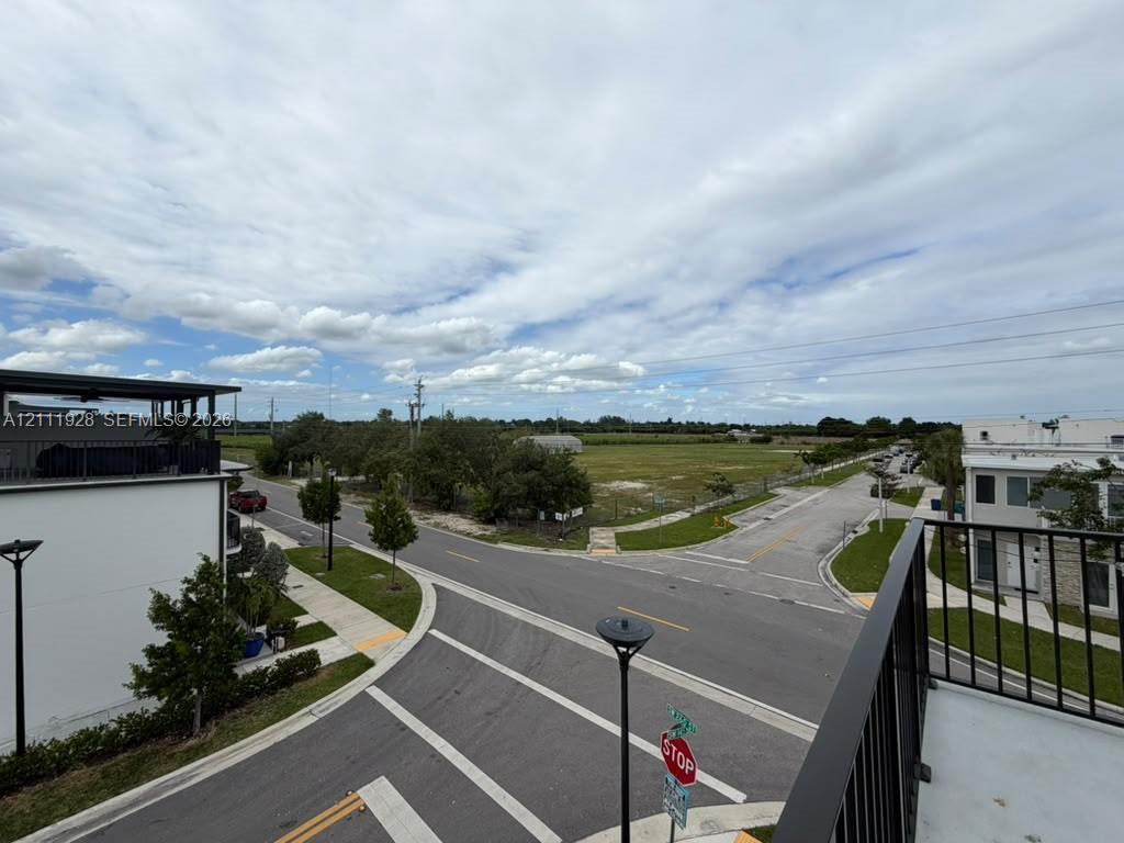 Elevated balcony featuring black metal railings and concrete flooring, overlooking an intersection with paved streets, concrete sidewalks, and street lighting