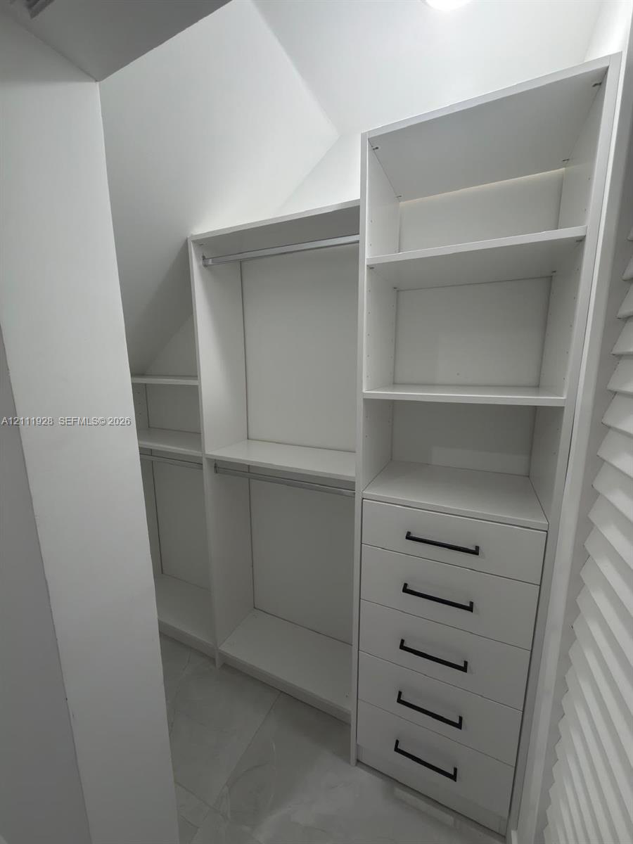 Custom walk-in closet featuring white built-in shelving, a five-drawer dresser unit, hanging rods, and matte black hardware