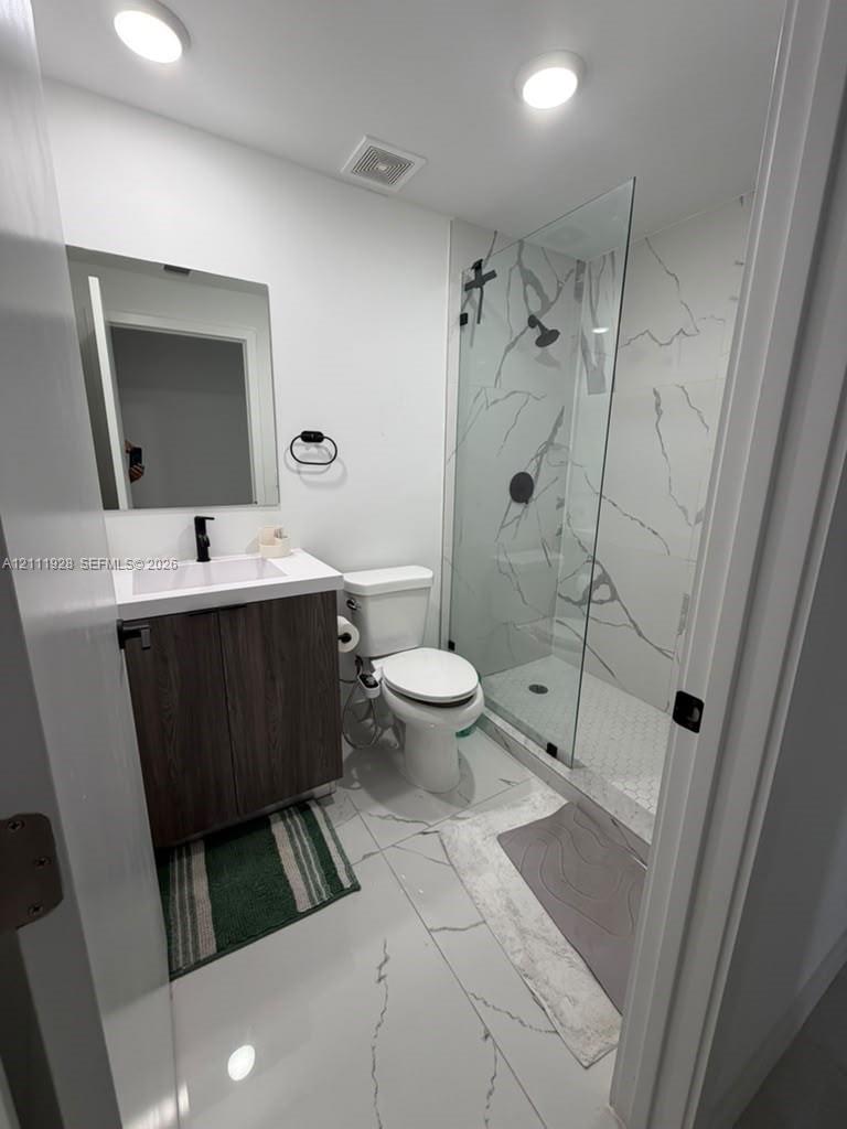 Bathroom featuring a glass-enclosed shower with floor-to-ceiling stone-style wall tile, white vanity with dark wood-finish cabinetry, rectangular vessel sink, and matte black fixtures