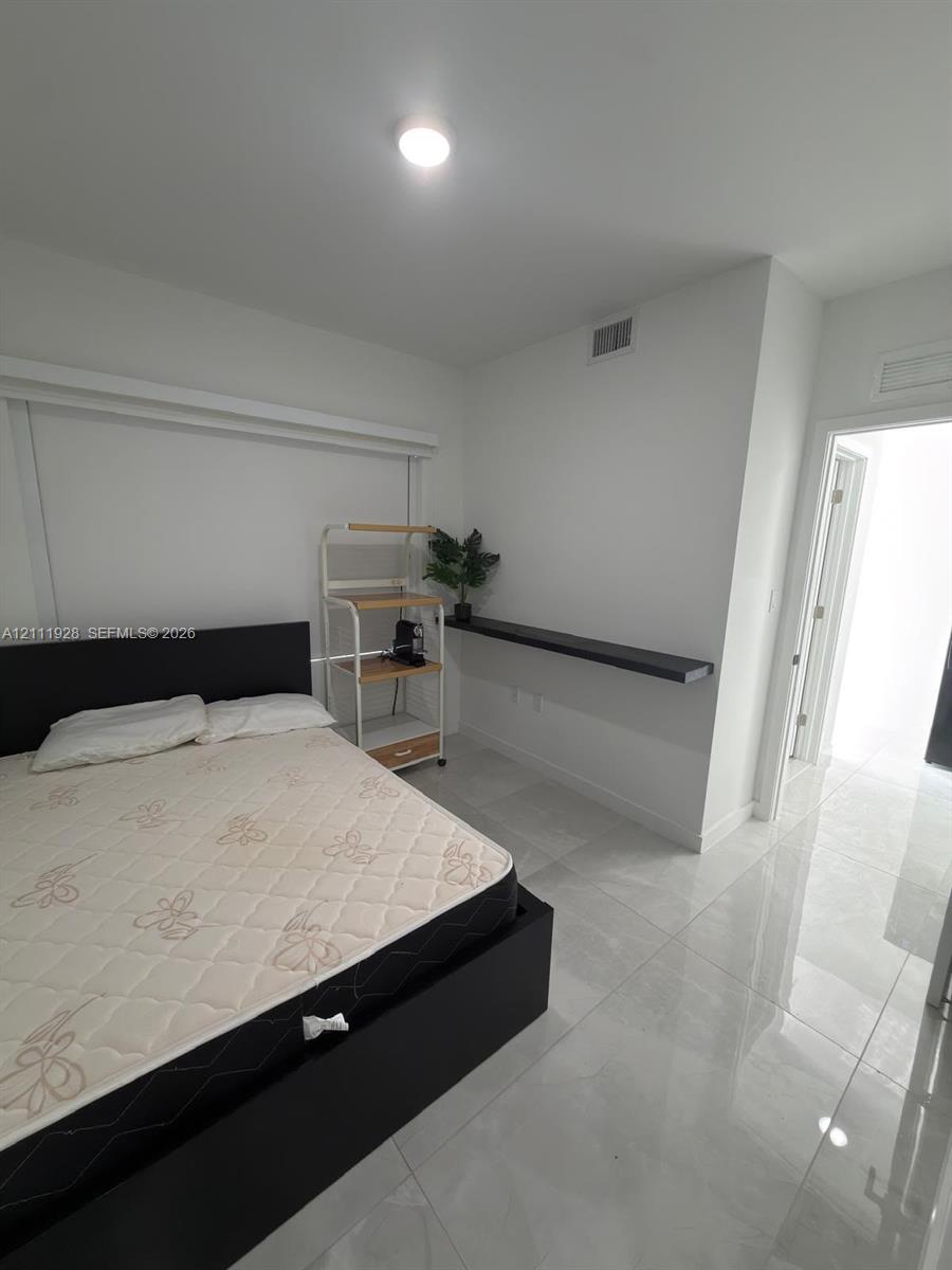 Neutral interior room featuring large-format tile flooring, a wall-mounted floating shelf, and a recessed ceiling light fixture