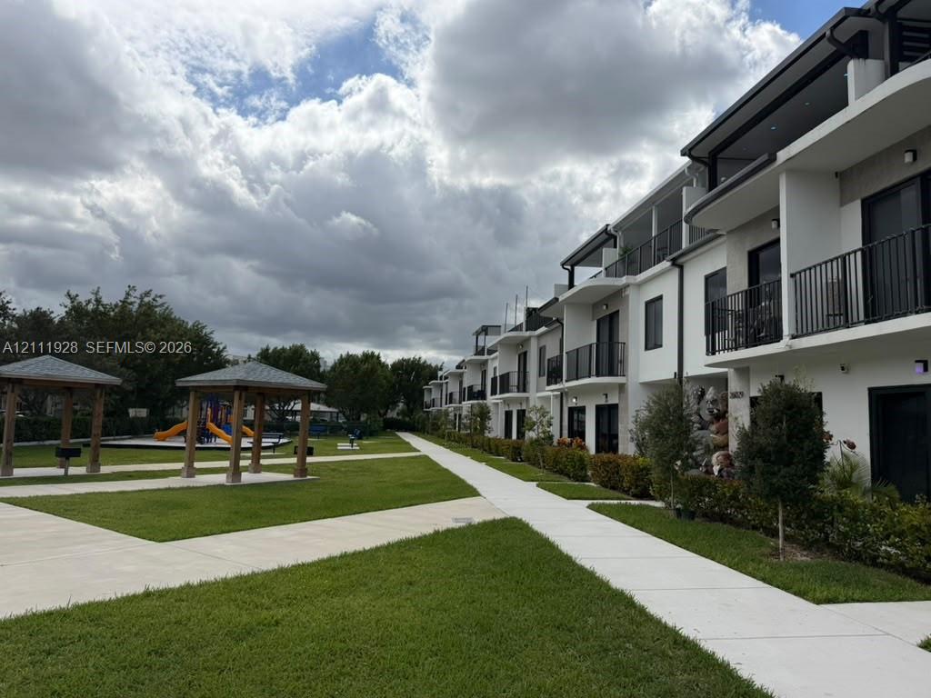 Multi-story exterior featuring white stucco siding, private balconies with metal railings, paved walkways, and detached wood-frame gazebos situated on manicured grounds