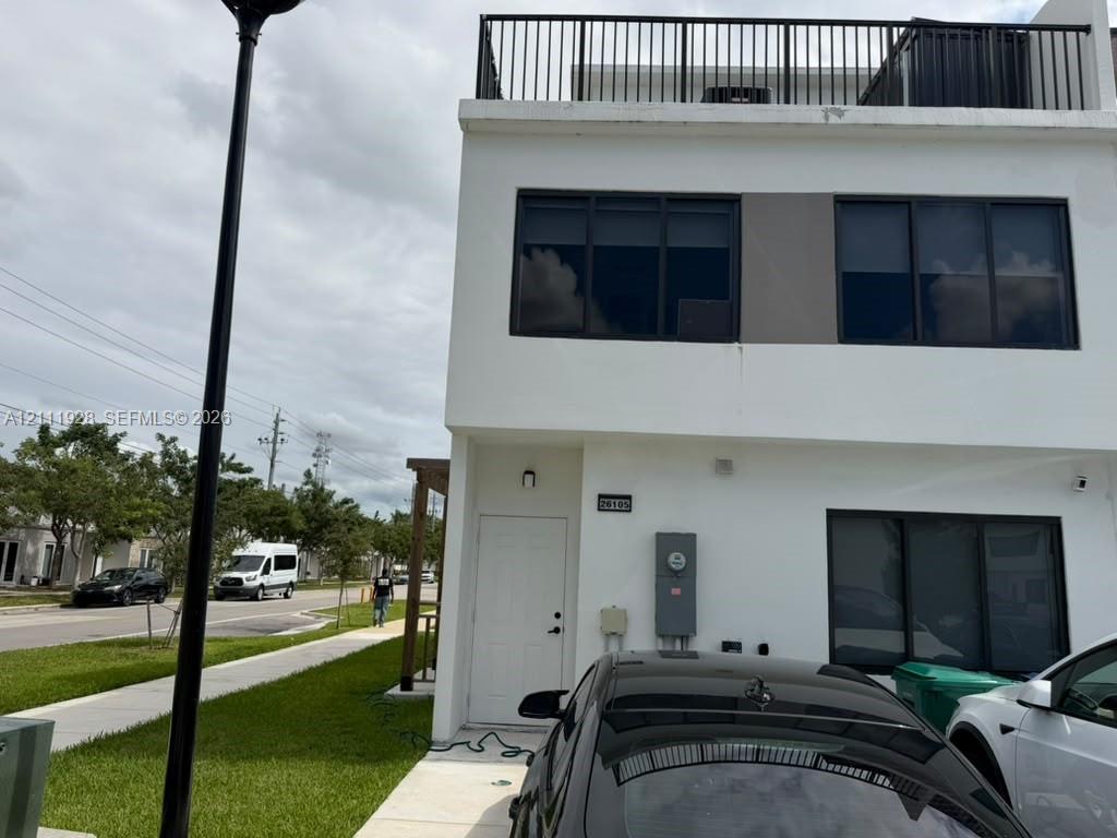 Contemporary exterior featuring a white smooth-stucco facade, flat roofline, third-level terrace with metal railing, and dark-framed multi-pane windows