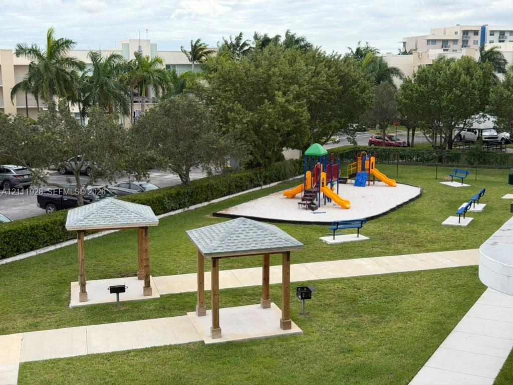 Common area featuring a playground with slides, two shaded pergolas, built-in outdoor grills, concrete walkways, and mature landscaping