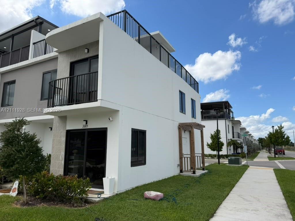 Modern townhome exterior featuring a rooftop deck with metal railings, a private second-story balcony, sliding glass doors, and a decorative wood-post entryway