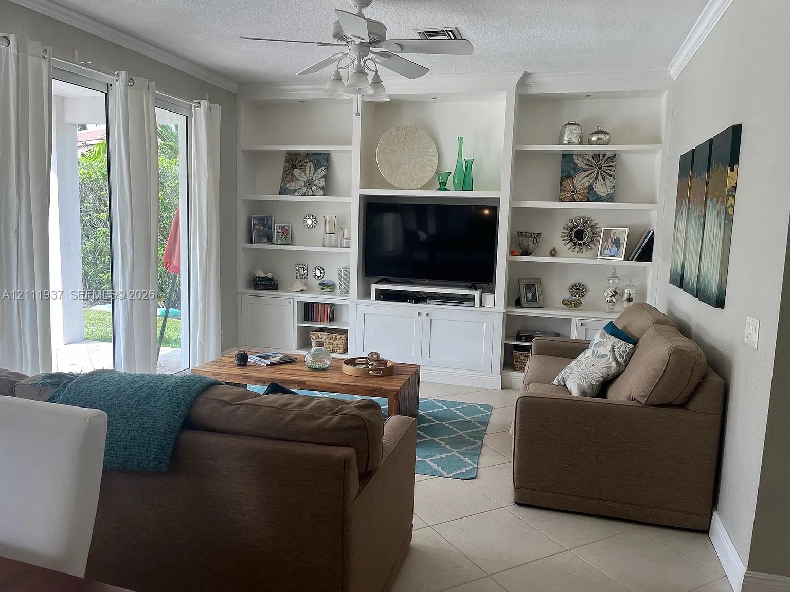 Built-in white cabinetry featuring recessed shelving and lower closed storage, neutral tile flooring, crown molding, and sliding glass doors