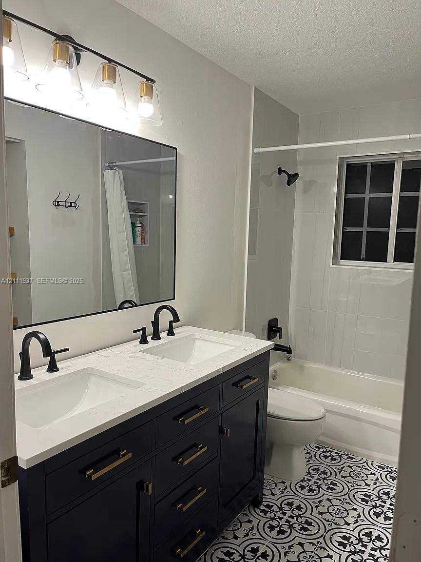 Double vanity with a white countertop and dark blue cabinetry, featuring matte black hardware, a geometric-patterned tile floor, and a four-light vanity fixture