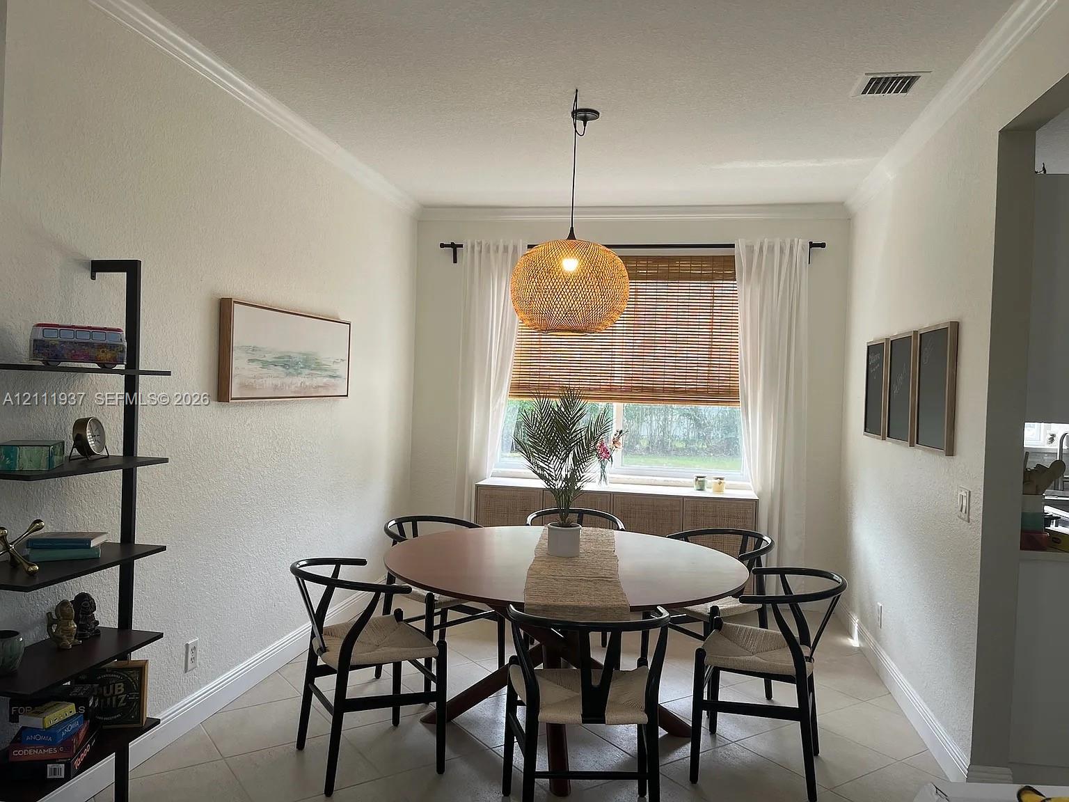Neutral interior space featuring tile flooring, crown molding, a woven pendant light fixture, and a window with a woven bamboo shade