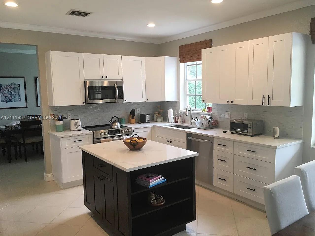 Kitchen featuring white shaker-style cabinetry, contrasting dark-toned kitchen island with open shelving, neutral-toned stone countertops, subway tile backsplash, and stainless steel appliances