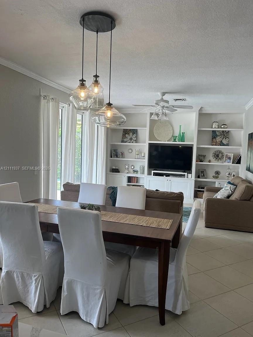 Built-in floor-to-ceiling shelving and cabinetry, three-light glass pendant fixture, neutral tile flooring, and ceiling fan