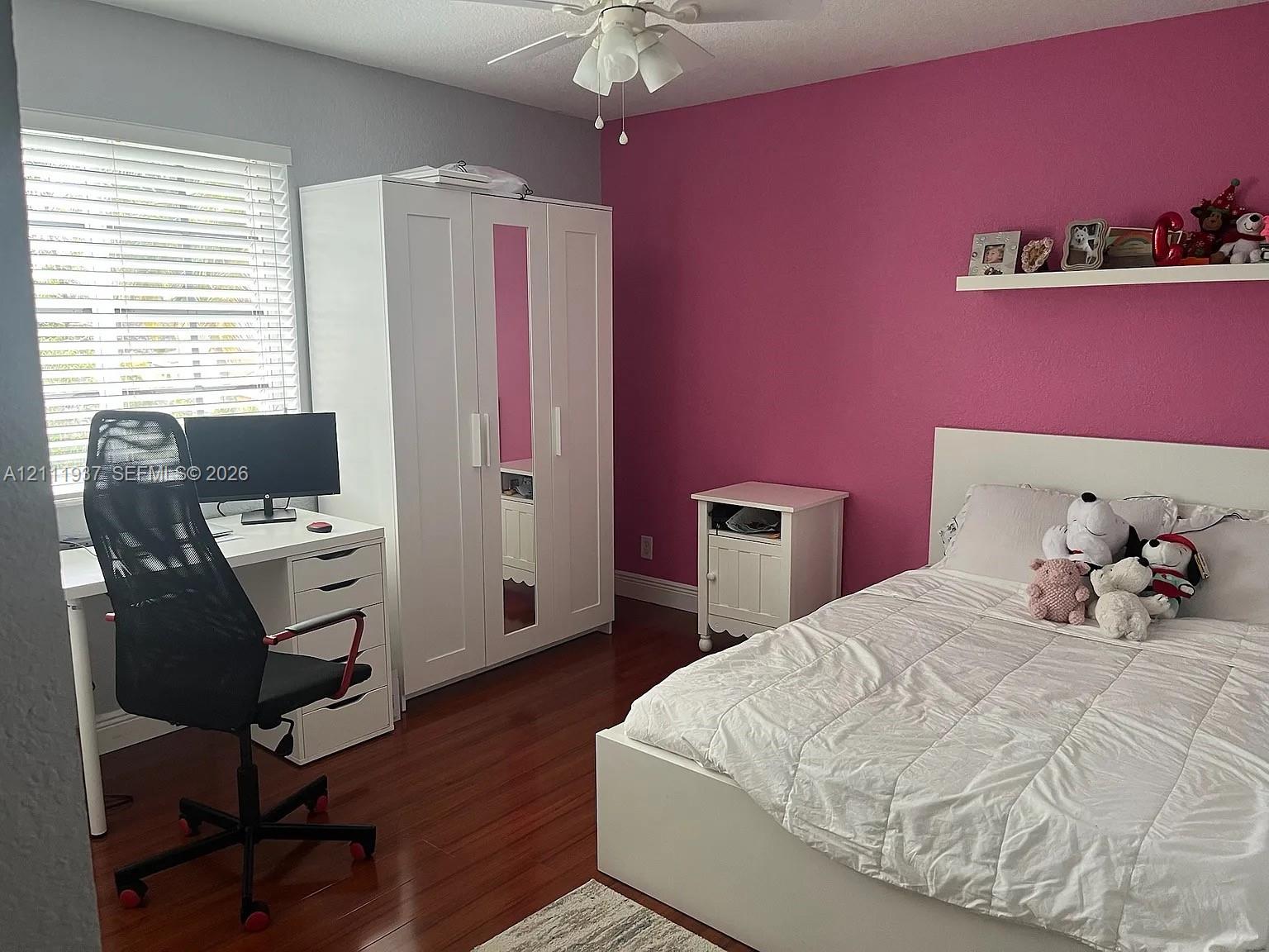 Wood-finish flooring, white built-in armoire with mirrored door, wall-mounted display shelf, and horizontal window blinds