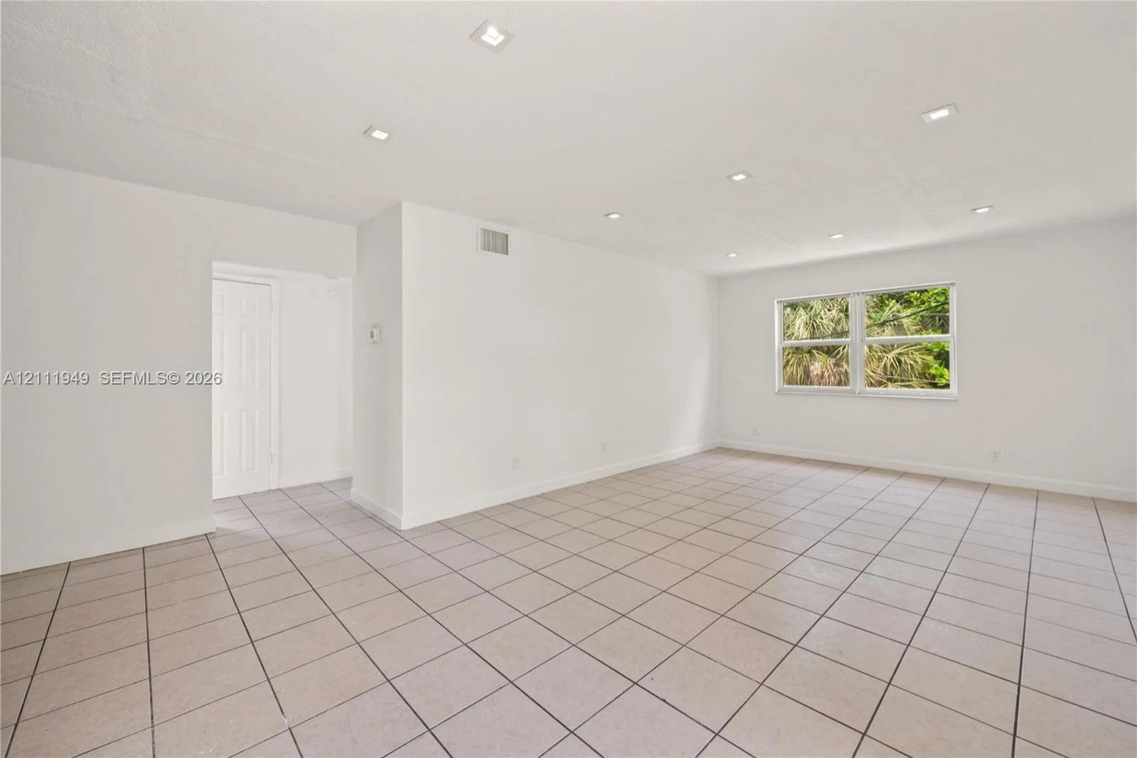 Open interior space featuring neutral ceramic tile flooring, recessed ceiling lighting, and a single-pane window