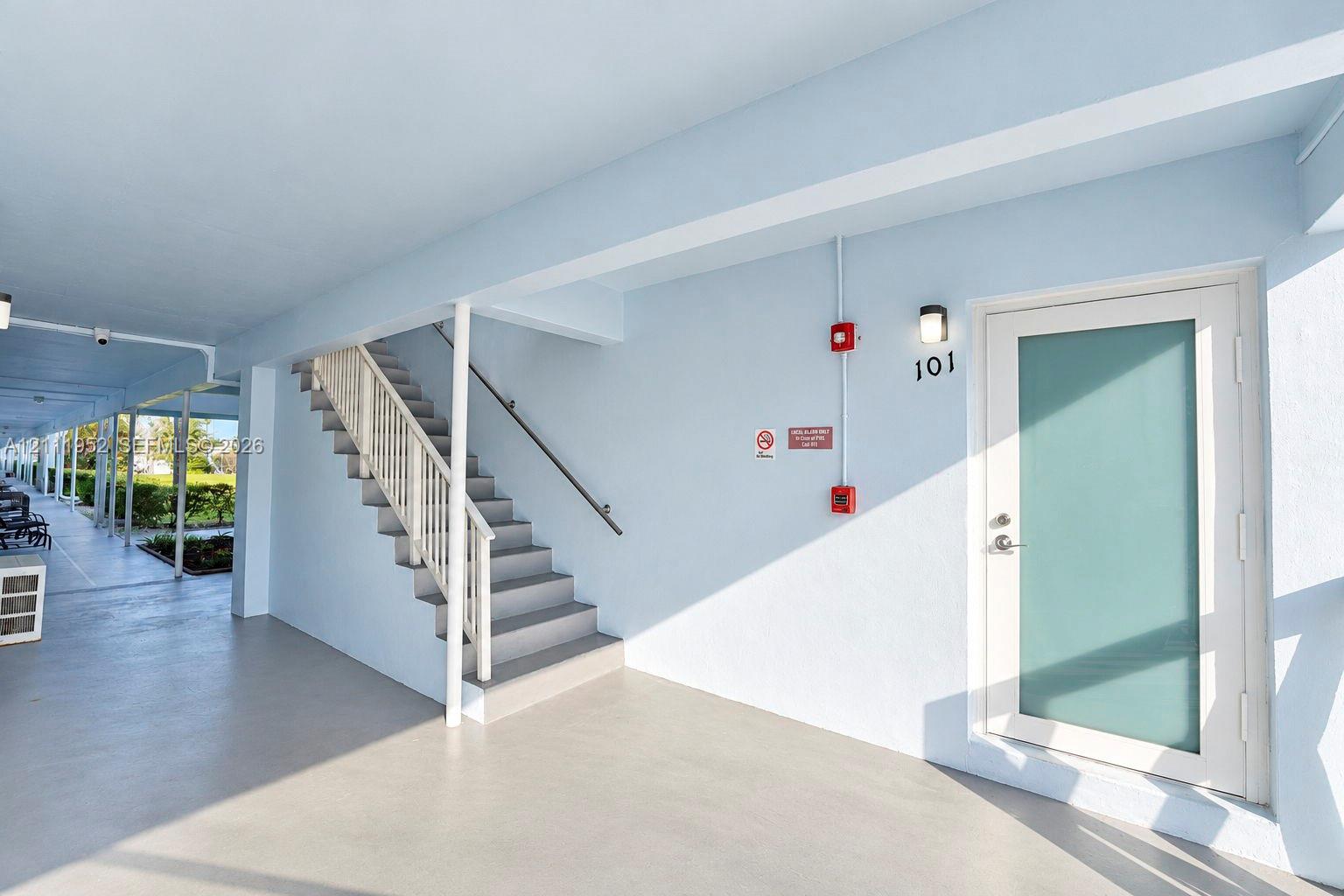 Covered entryway featuring a frosted impact glass entry door, painted concrete flooring, and an exterior staircase with metal railing