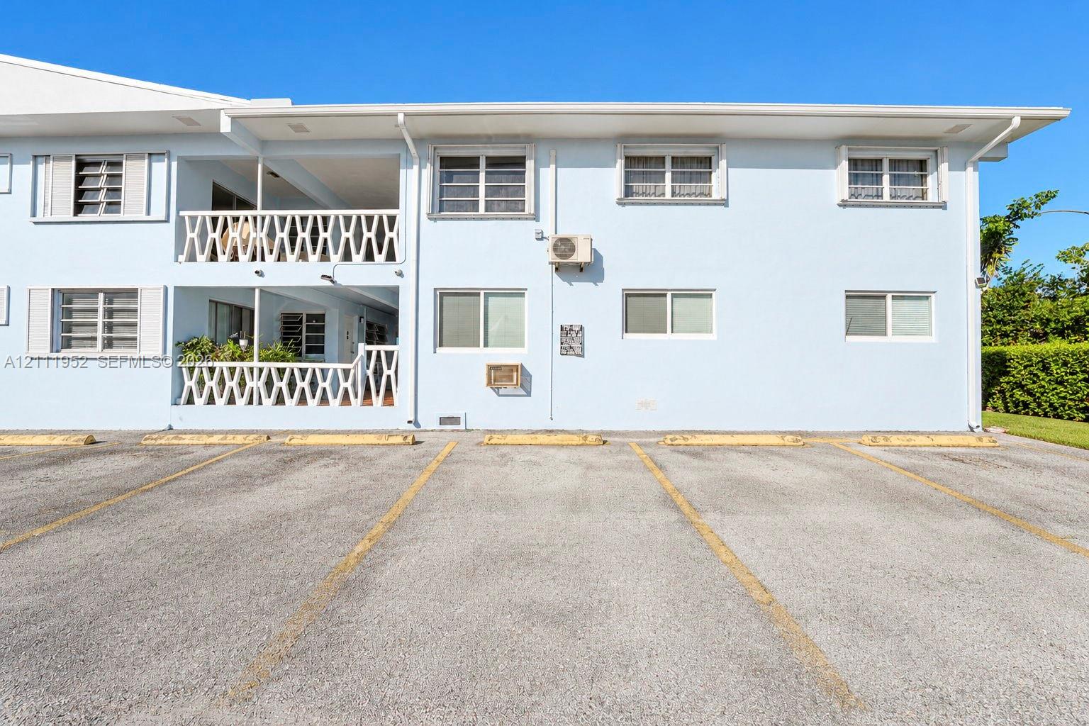 Multi-story exterior featuring a two-level railed balcony, asphalt parking area, and horizontal sliding windows