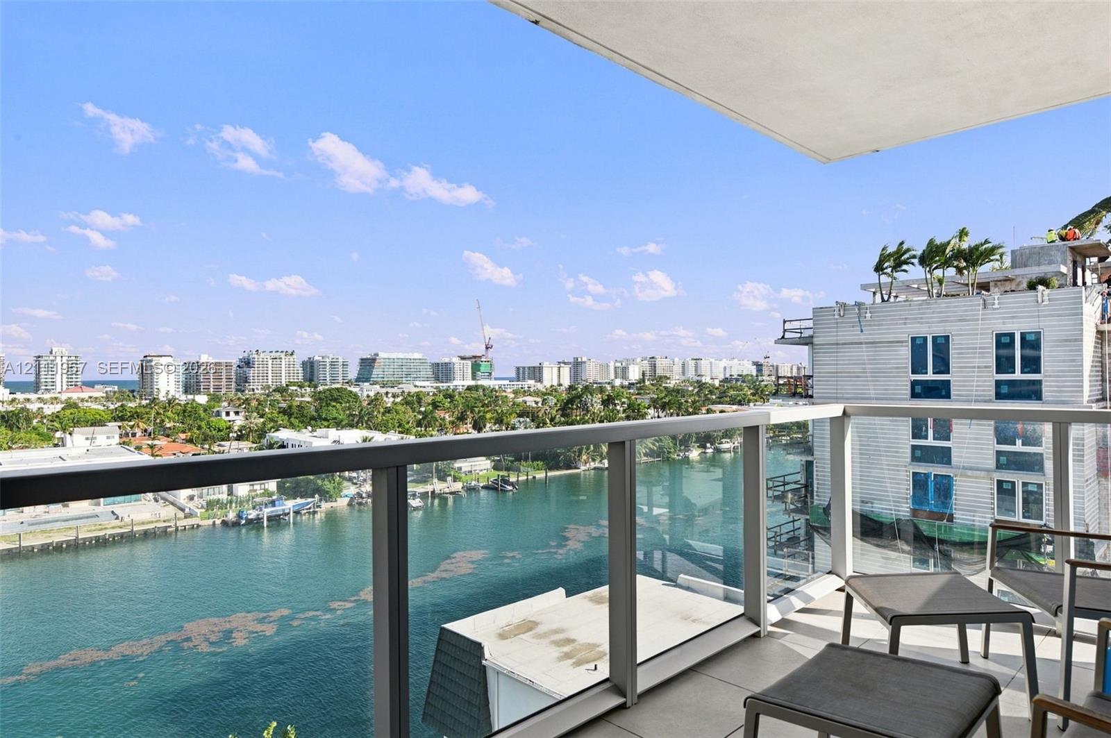 Covered balcony featuring a glass panel railing, tiled flooring, and expansive water and urban scenery