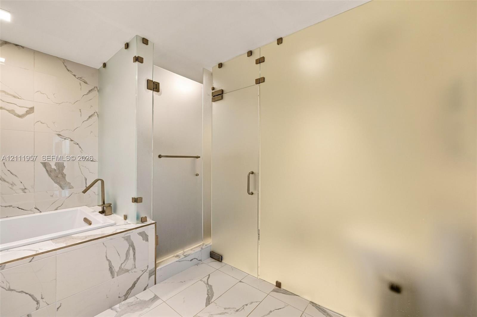 Soaking tub with a wall-mounted faucet, large-format stone-patterned tile flooring and wall cladding, and frosted glass partition walls with integrated hardware