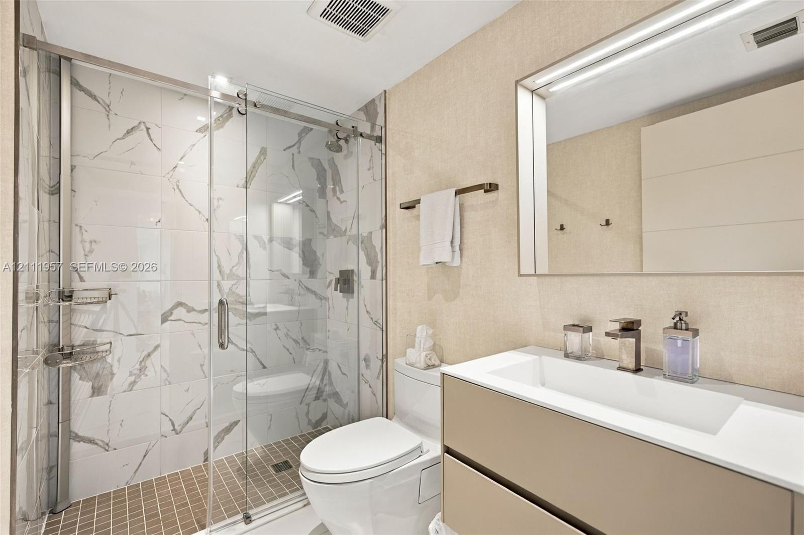 Floating vanity with integrated rectangular sink and metallic faucet, complemented by a walk-in shower featuring sliding glass doors and large-format veined tile surround