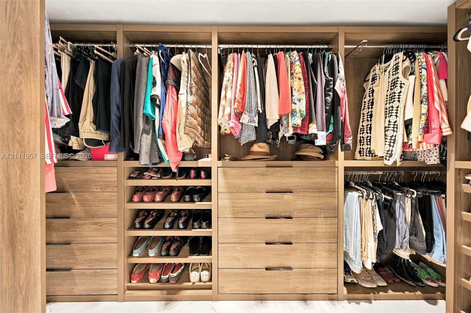 Custom closet organization system featuring wood-finish cabinetry, multi-tiered hanging rods, integrated shelving for footwear, and deep drawers with modern hardware