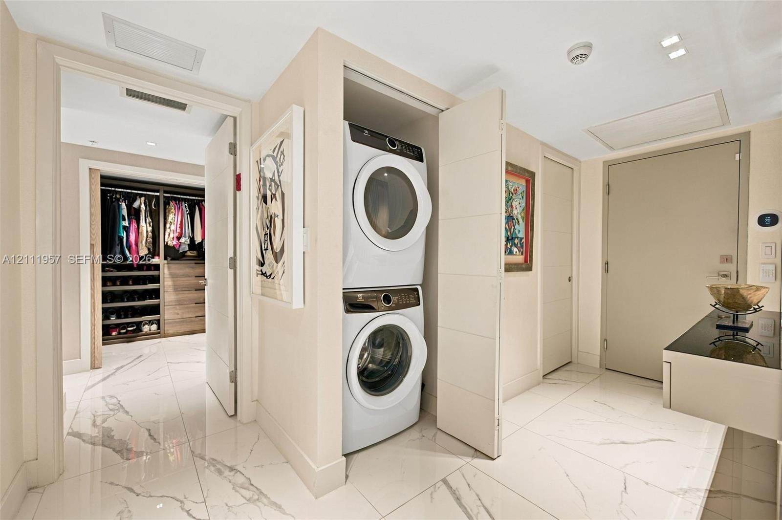 Stacked laundry unit housed in a dedicated closet, polished stone-finish flooring, and built-in closet shelving with integrated drawers