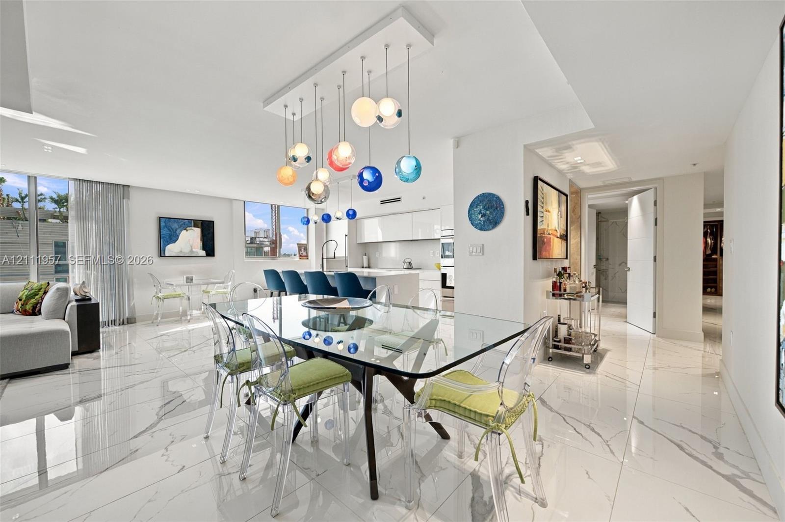 Large format tile flooring with high-gloss finish, multi-colored tiered glass globe chandelier, expansive floor-to-ceiling windows, and minimalist kitchen cabinetry Large format tile flooring with high-gloss finish, multi-colored tiered glass globe chandelier, expansive floor-to-ceiling windows, and minimalist kitchen cabinetry