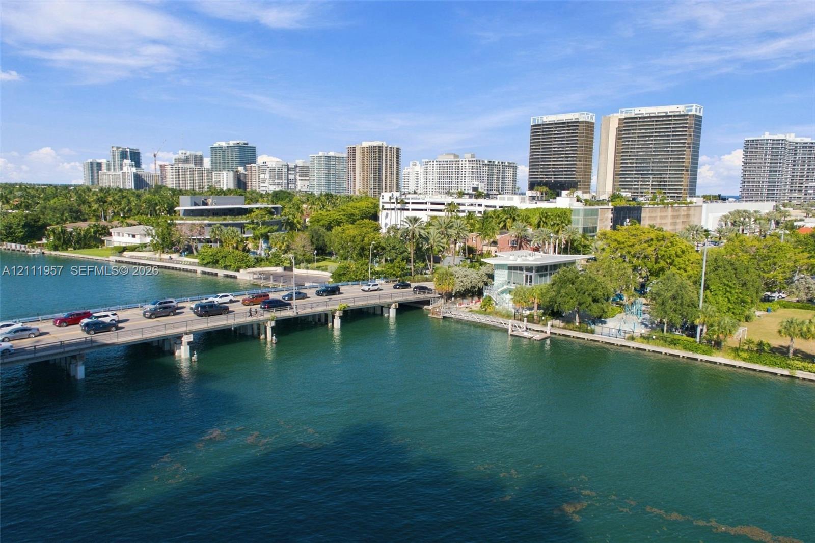 Aerial perspective featuring a waterfront setting, boat dock, mature landscaping, and an expansive bridge spanning the waterway