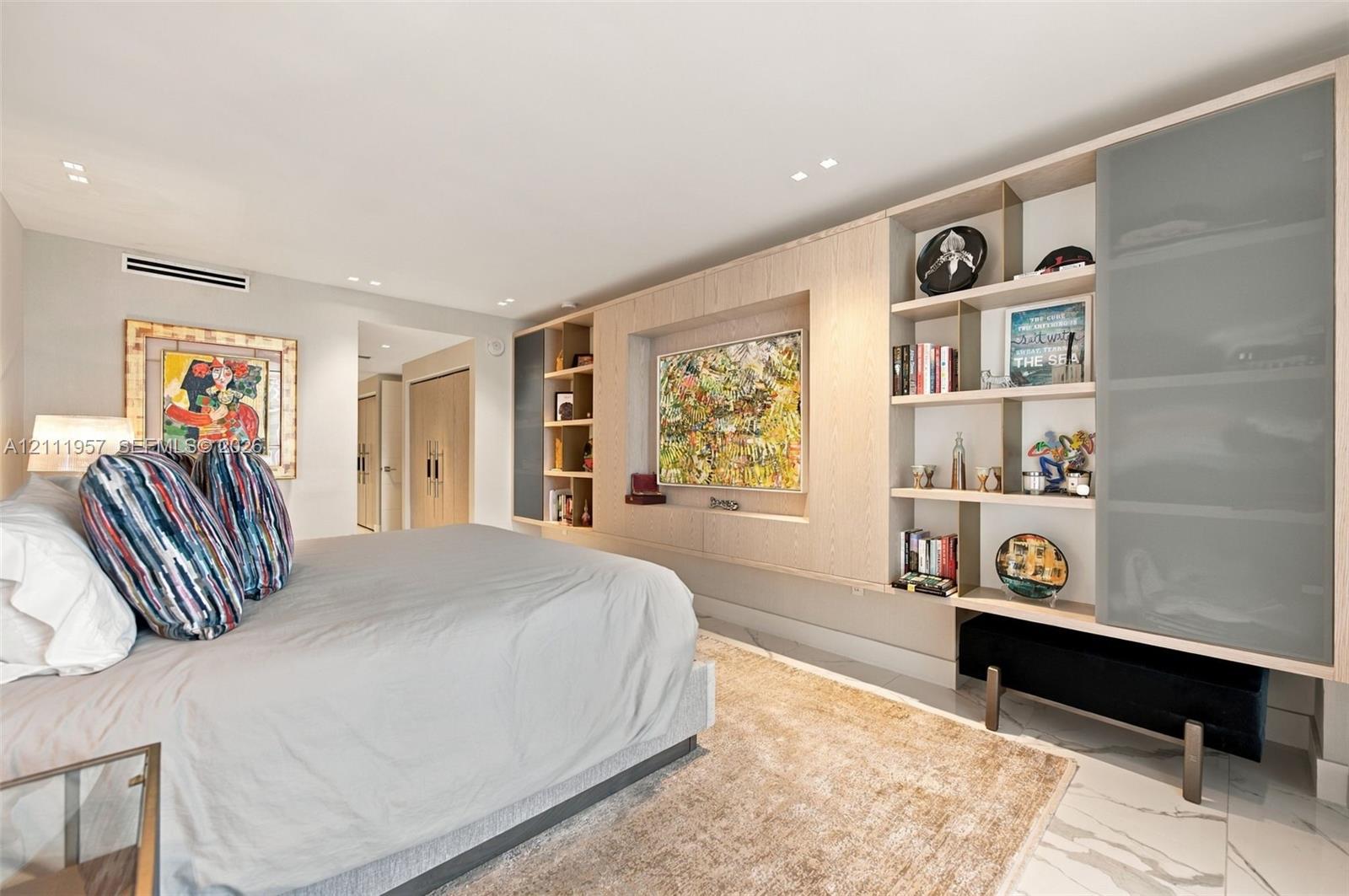 Built-in light wood cabinetry featuring open display shelving and recessed television mount, stone-finish flooring, and recessed ceiling lighting