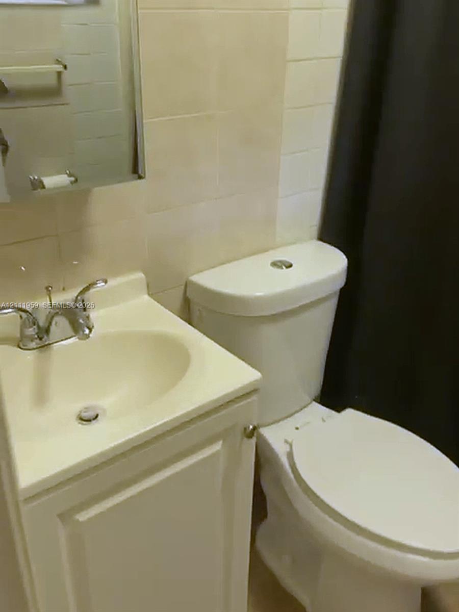 Bathroom featuring a white vanity cabinet with an integrated sink, dual-handle chrome faucet, wall-mounted medicine cabinet, and ceramic wall tiling