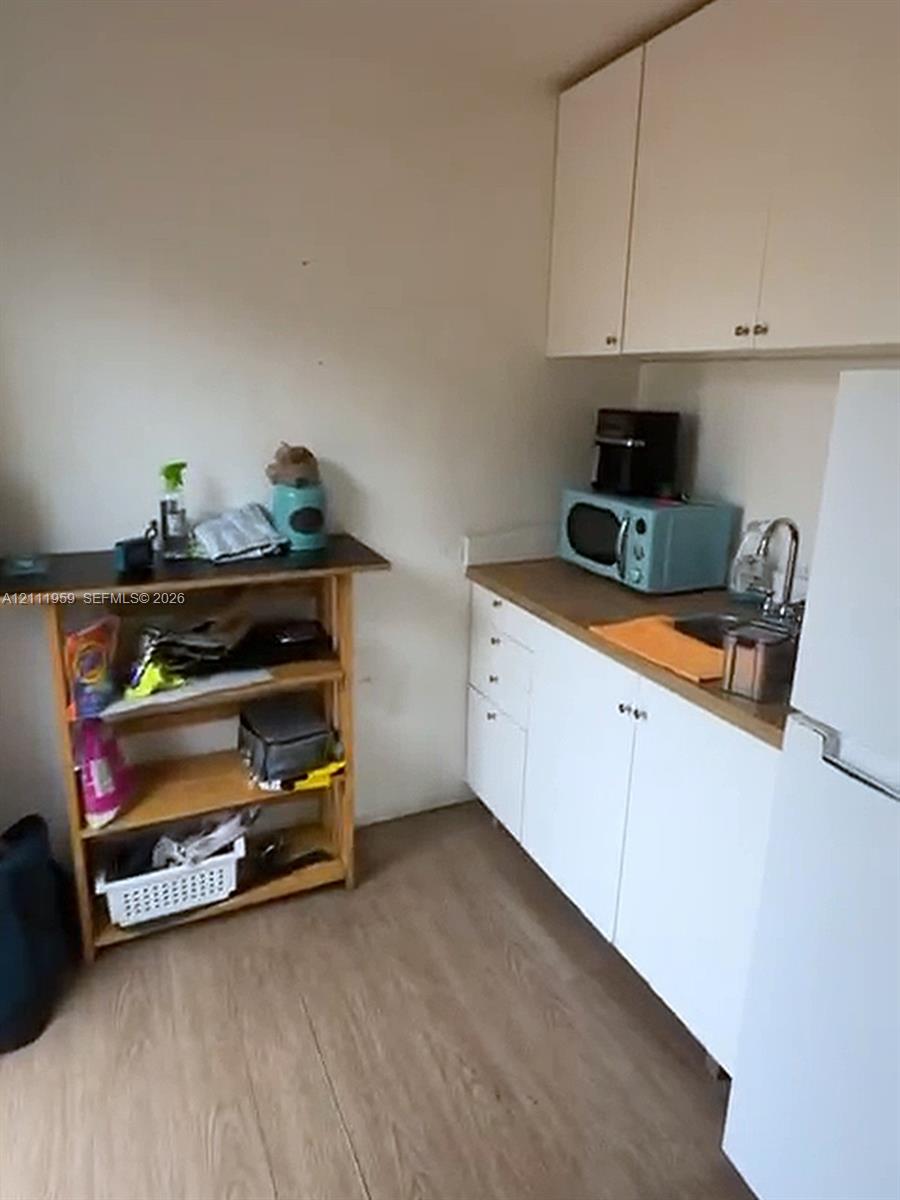Kitchenette area featuring white cabinetry, wood-finish flooring, and a stainless steel sink with a high-arch faucet