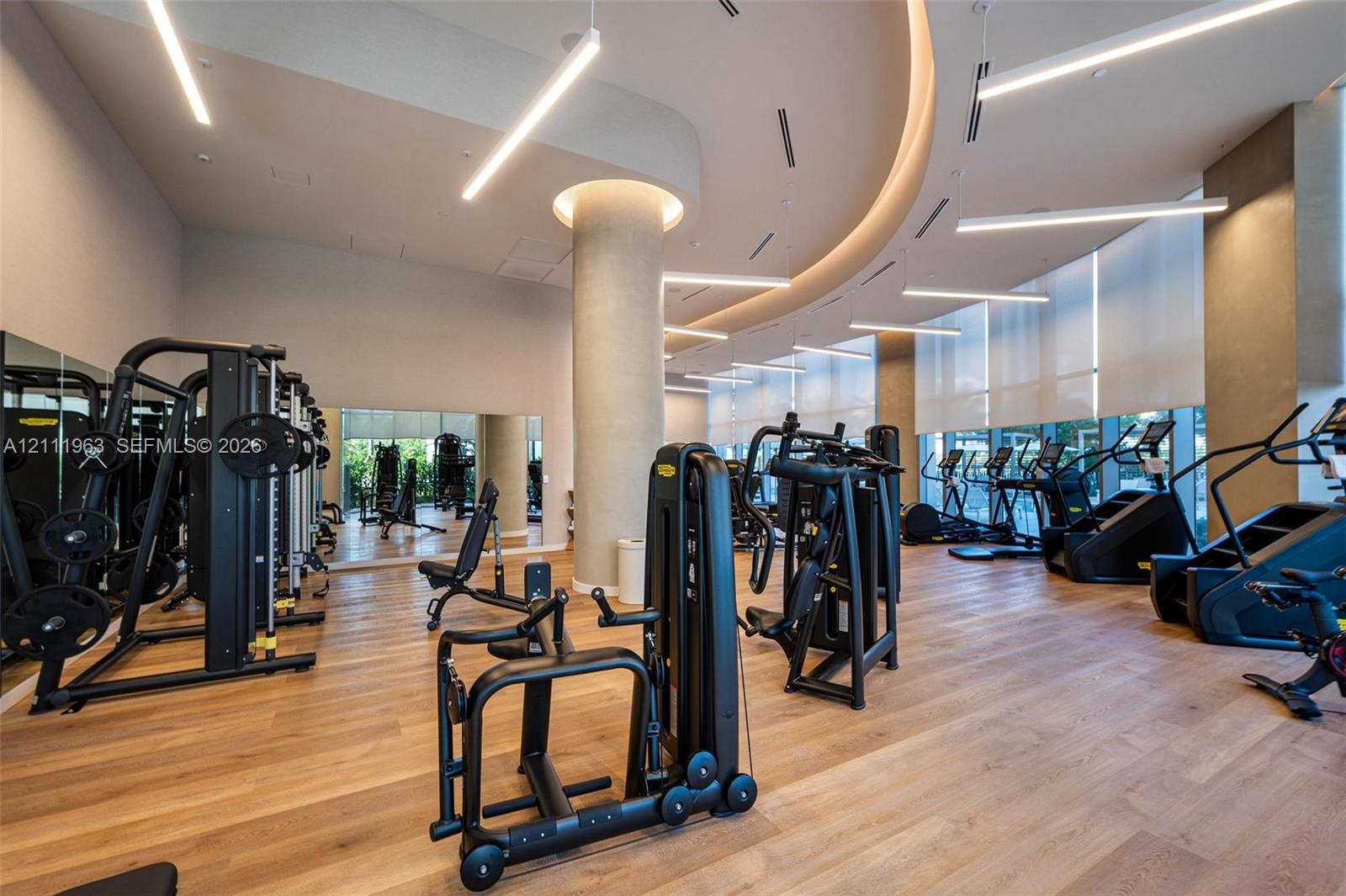 Fitness facility featuring floor-to-ceiling windows, wood-finish flooring, recessed tray ceiling lighting, and large wall-mounted mirrors