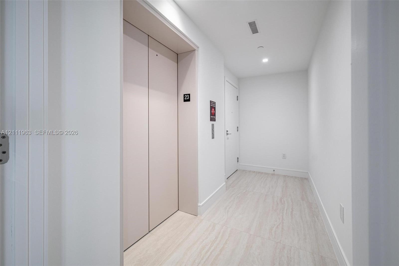 Hallway featuring neutral-toned stone-finish flooring, recessed ceiling lighting, and dedicated elevator access