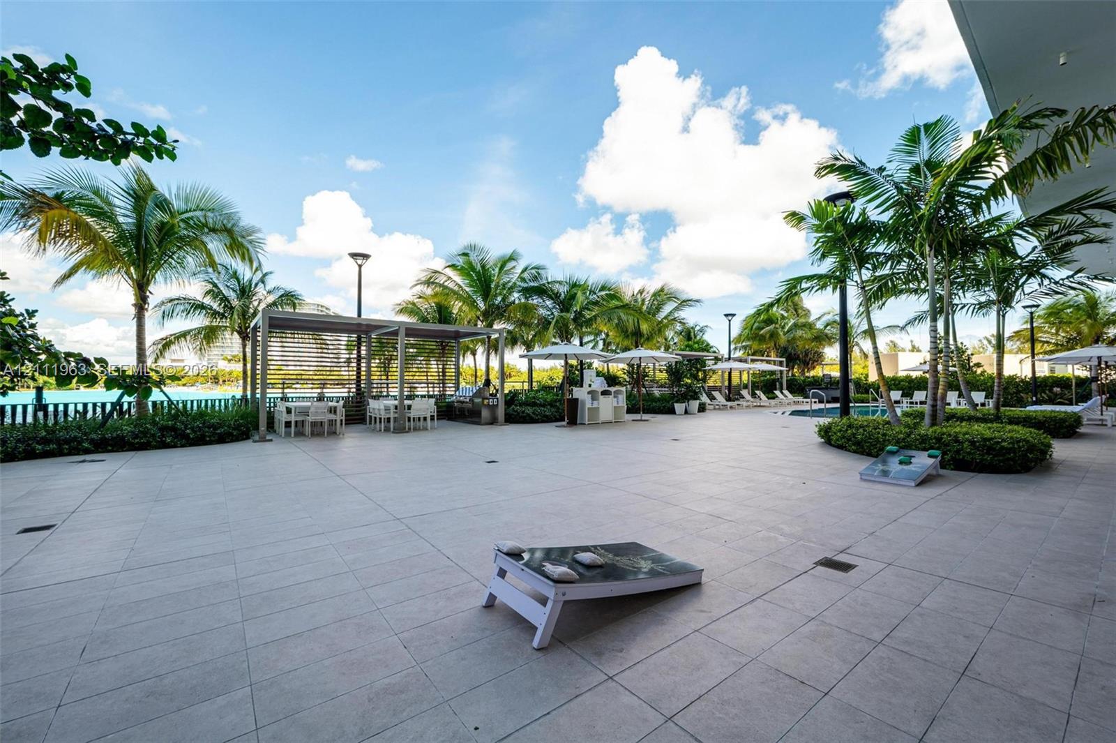 Outdoor terrace featuring large-format stone tile flooring, perimeter landscaping with mature palms, and a built-in white service station